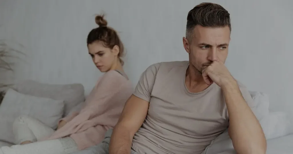 Man sitting turned away from his partner on the sofa, pushing his partner away