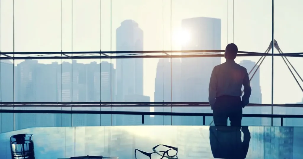 Man in an office looking out over a city skyline, feeling successful but unfulfilled